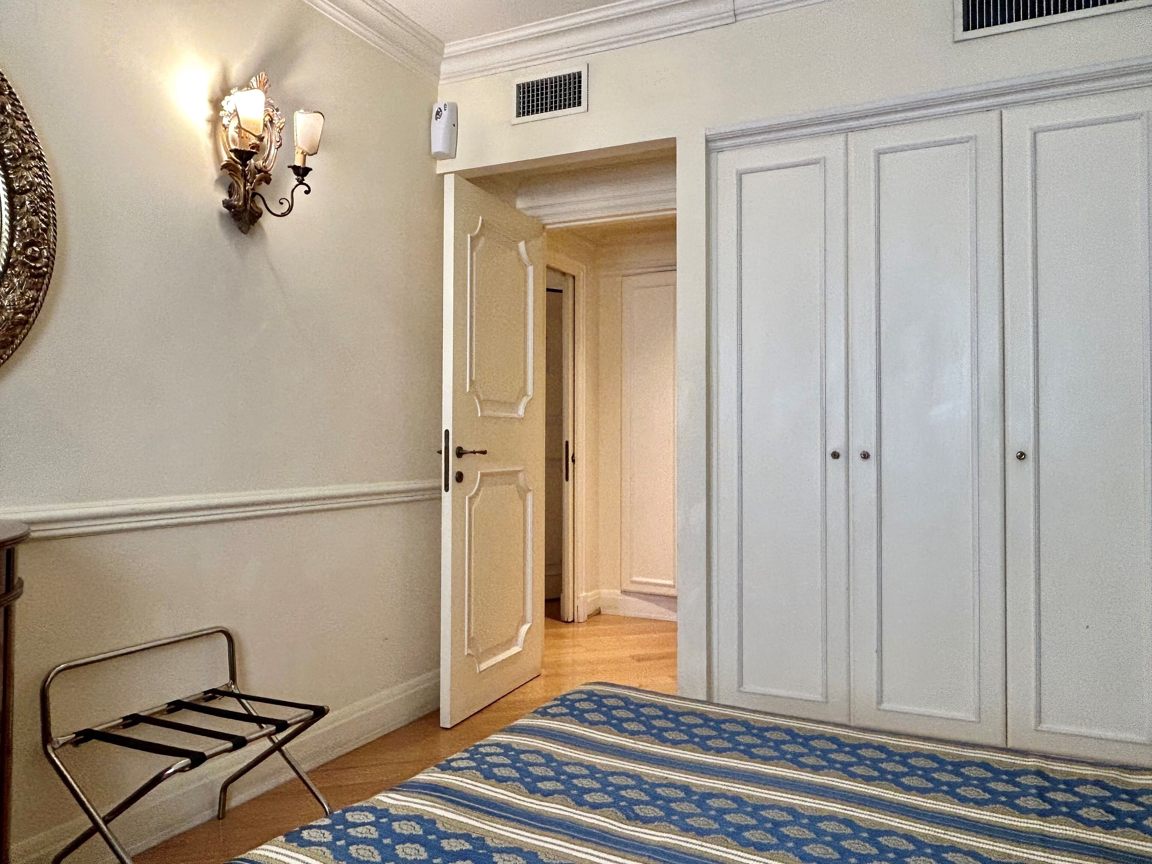 Une pièce comprenant un lit, un banc en métal, une armoire et un luminaire fixé au mur.