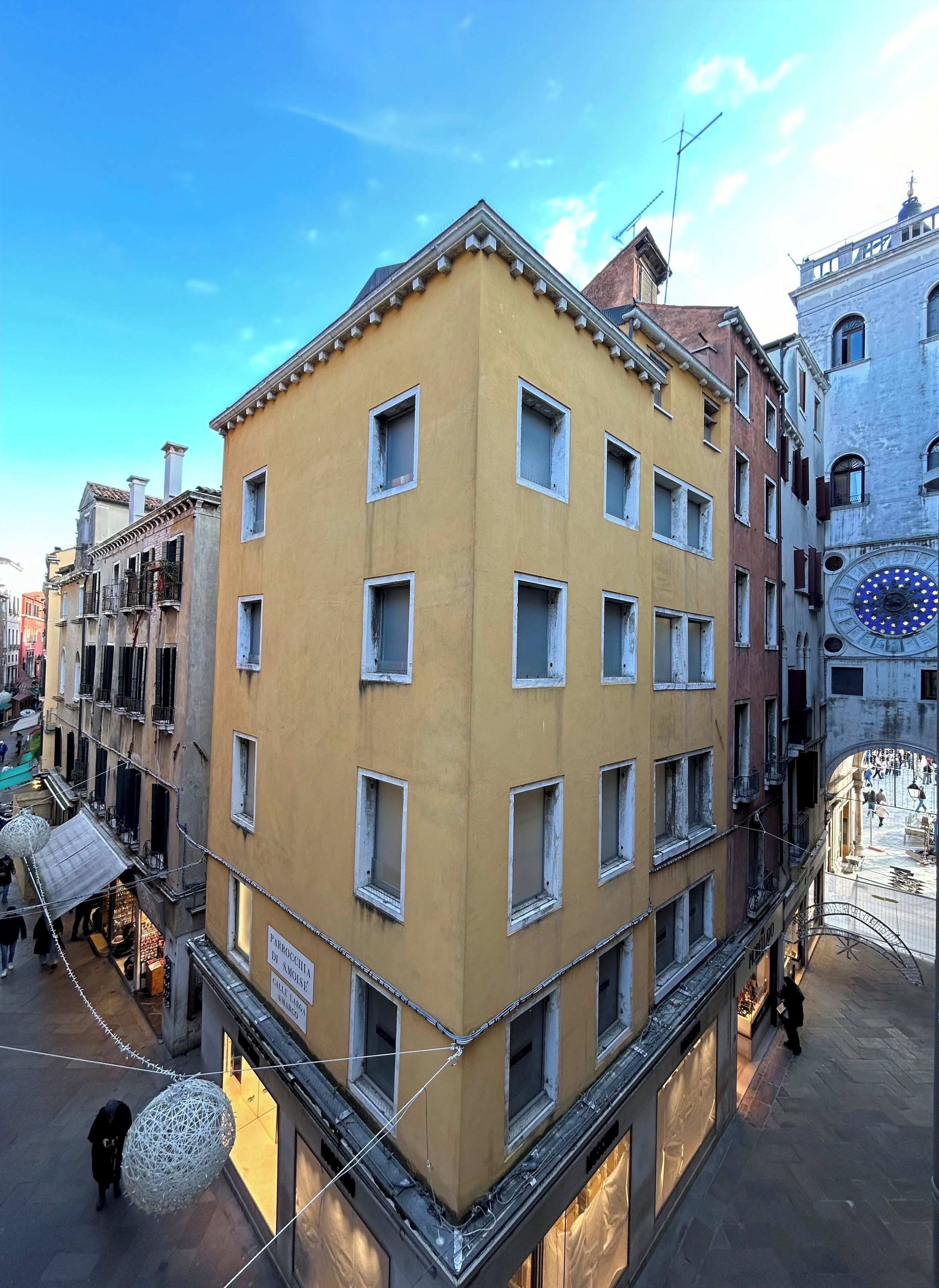 Un edificio de varios pisos con fachada amarilla, múltiples ventanas y una torre de reloj.