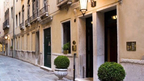 A narrow street with a building featuring balconies, a sign reading "HOTEL," and two potted plants. - TORRE DELL'OROLOGIO SIGNATURE RESIDENCE (Venice)