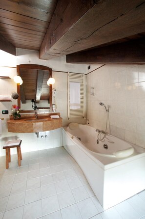 A bathroom with a wooden ceiling, a large bathtub, a vanity with a mirror, and a toilet. - Primotel (Brescia)