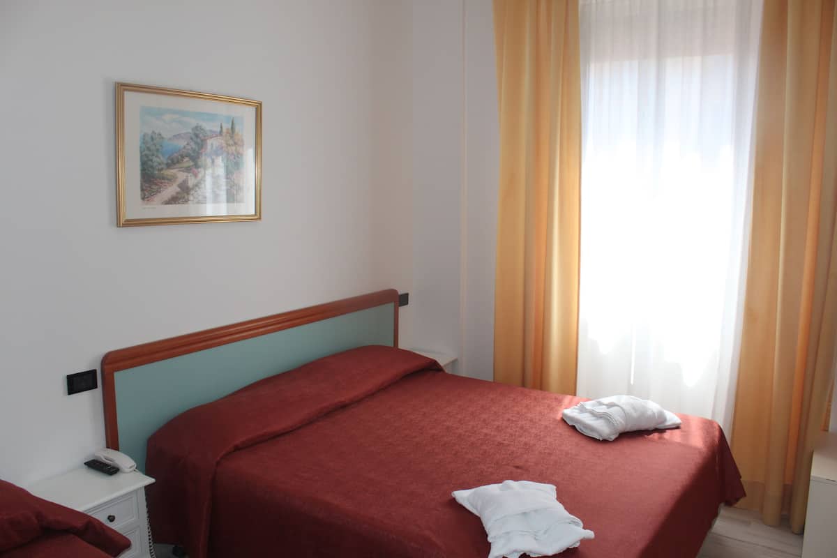 A hotel room with a bed, a bedside table with a phone, a framed picture on the wall, and a window with curtains.