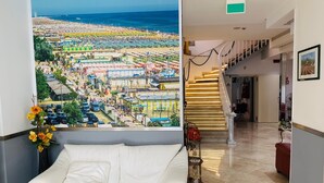 Un hall d’hôtel avec une grande fresque représentant une plage, un canapé blanc, un escalier et un tableau encadré au mur.