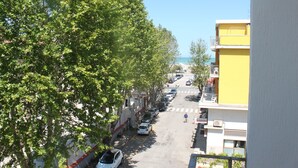 Une rue bordée de voitures garées et d’arbres, qui mène à un immeuble jaune doté de balcons.