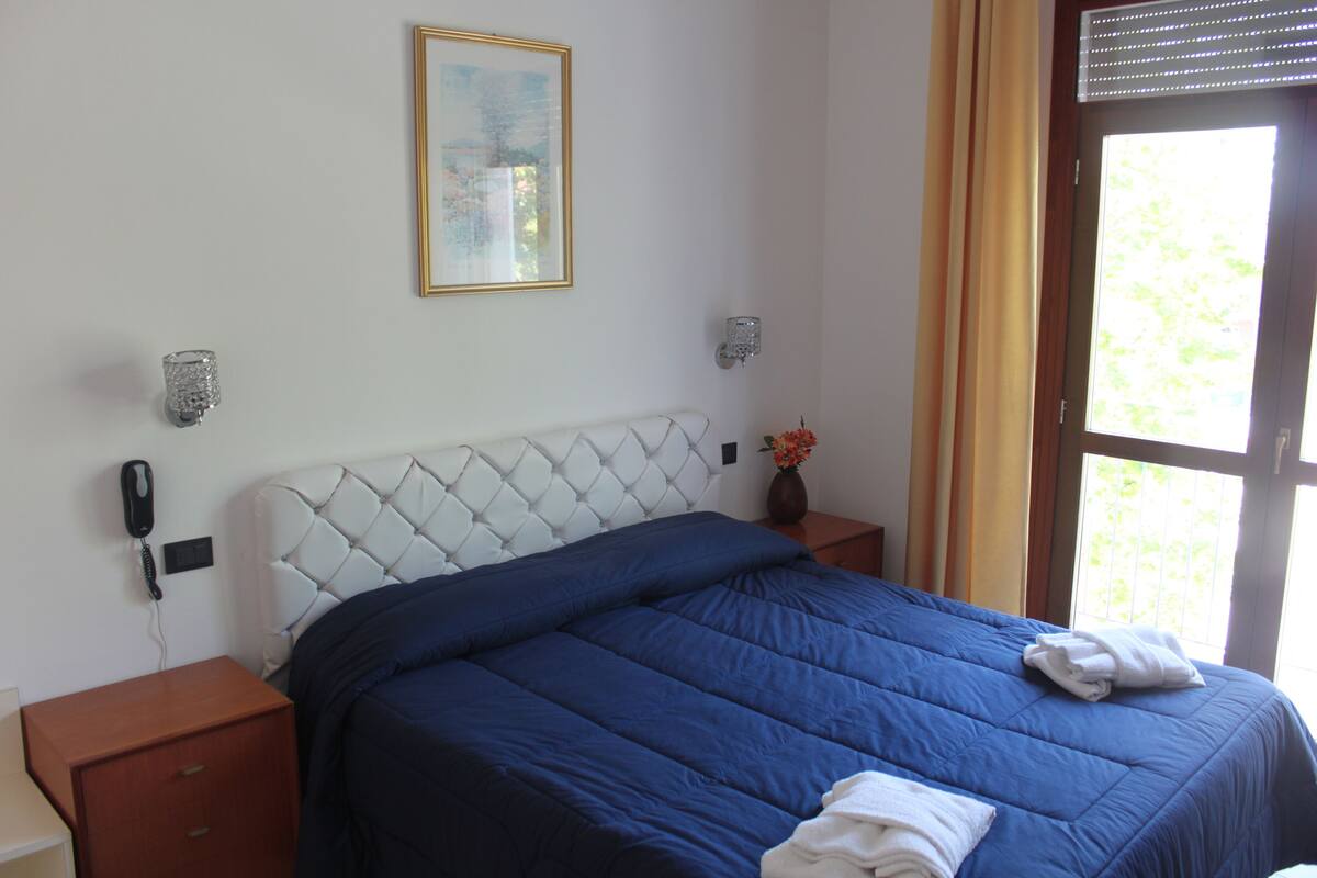 A bedroom with a large bed, a bedside table with a phone, a wall-mounted light, and a window with curtains.