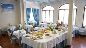 Une salle de banquet avec des tables rondes recouvertes de nappes blanches, des chaises bleues, ainsi qu’une variété de plats et de boissons.