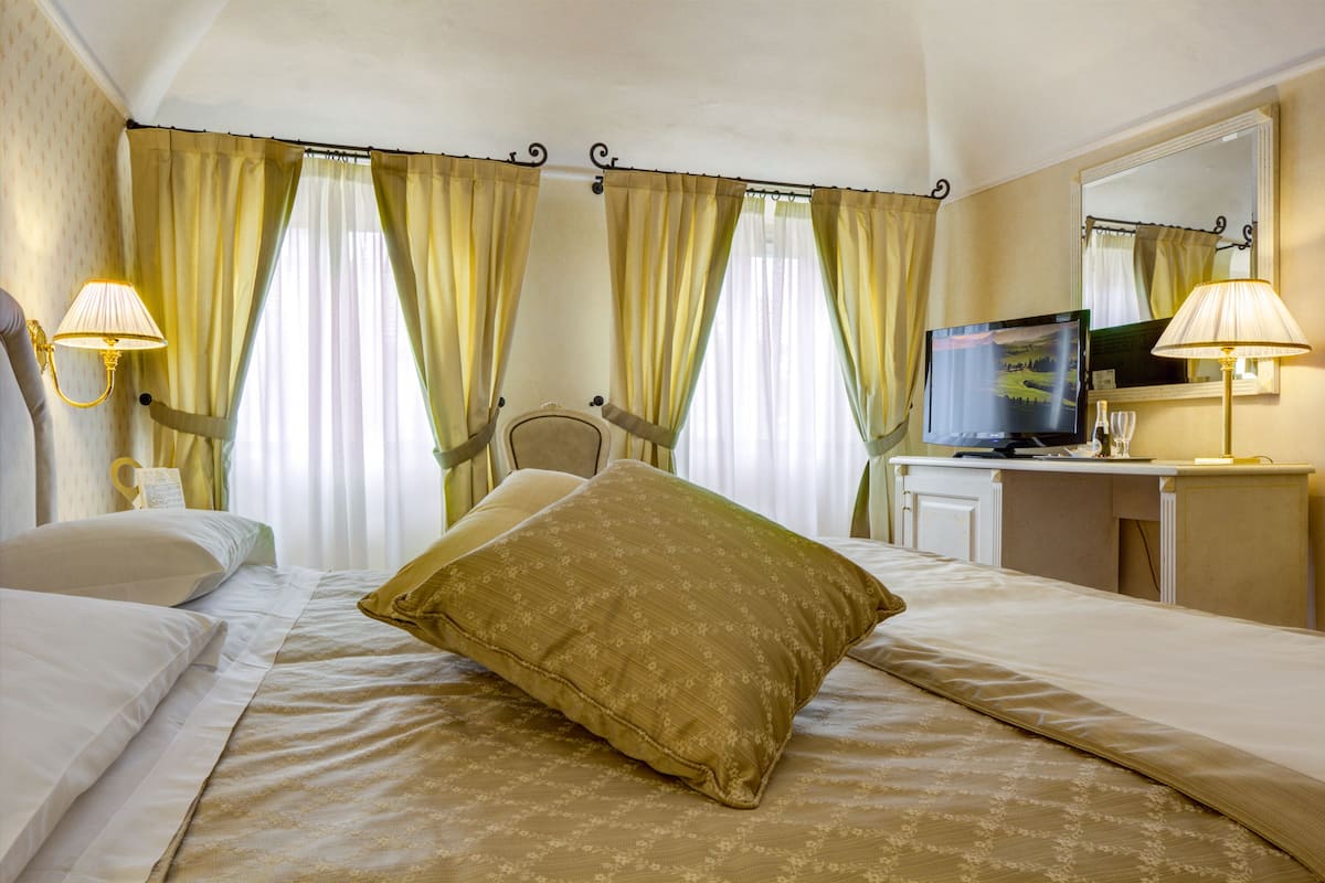 A hotel room with a bed, two bedside lamps, a television, and curtains.