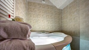 A bathroom with a bathtub, beige tiles, a rose, and towels. - Hotel La Locanda (Volterra)