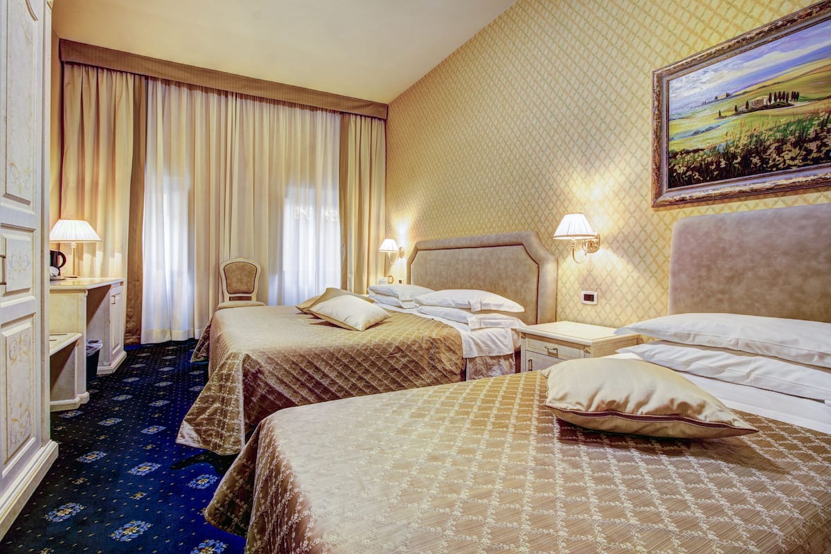 A hotel room with two beds, a desk, a chair, and a painting on the wall.