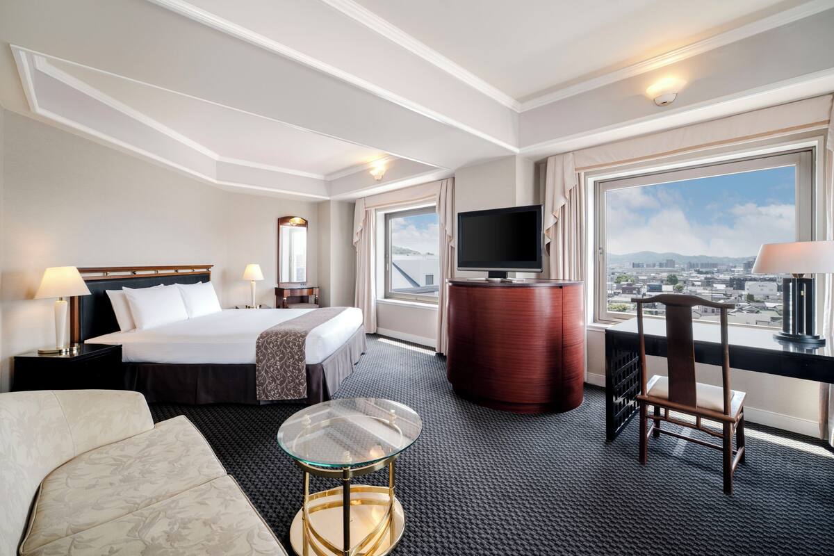 Une chambre d’hôtel avec un lit, une télévision, un bureau, une chaise et une vue sur la ville.