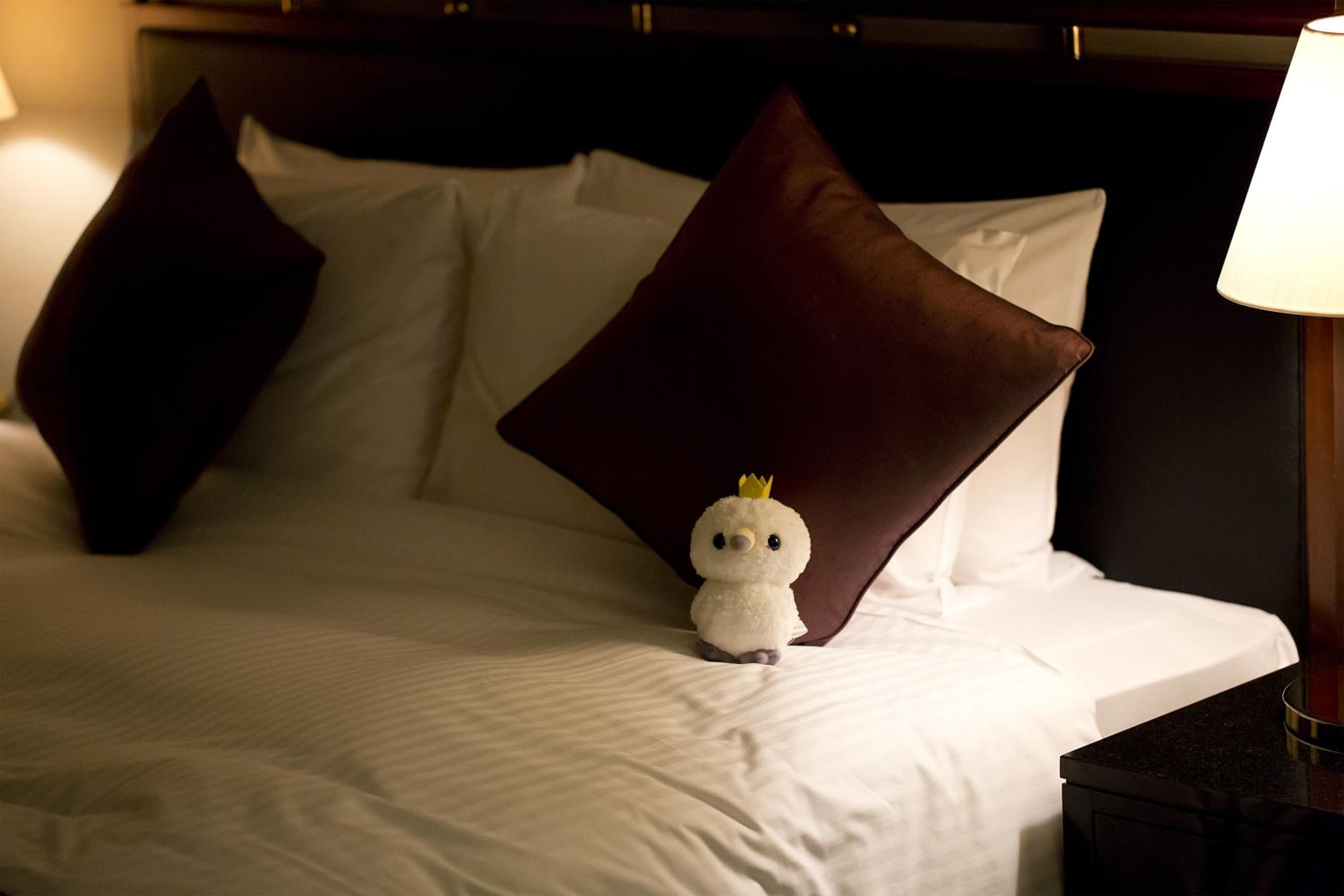 A neatly made bed with white linens and a single brown pillow.