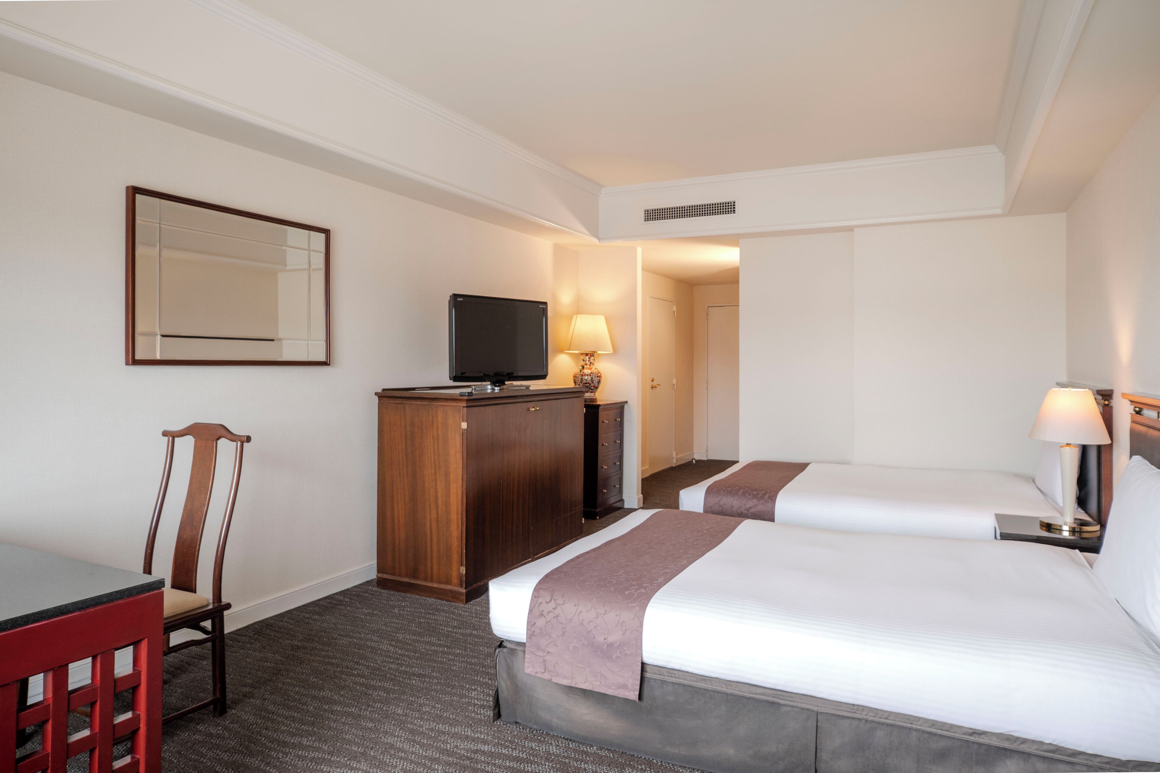 A hotel room with two beds, a desk, a chair, a television, and a mirror.