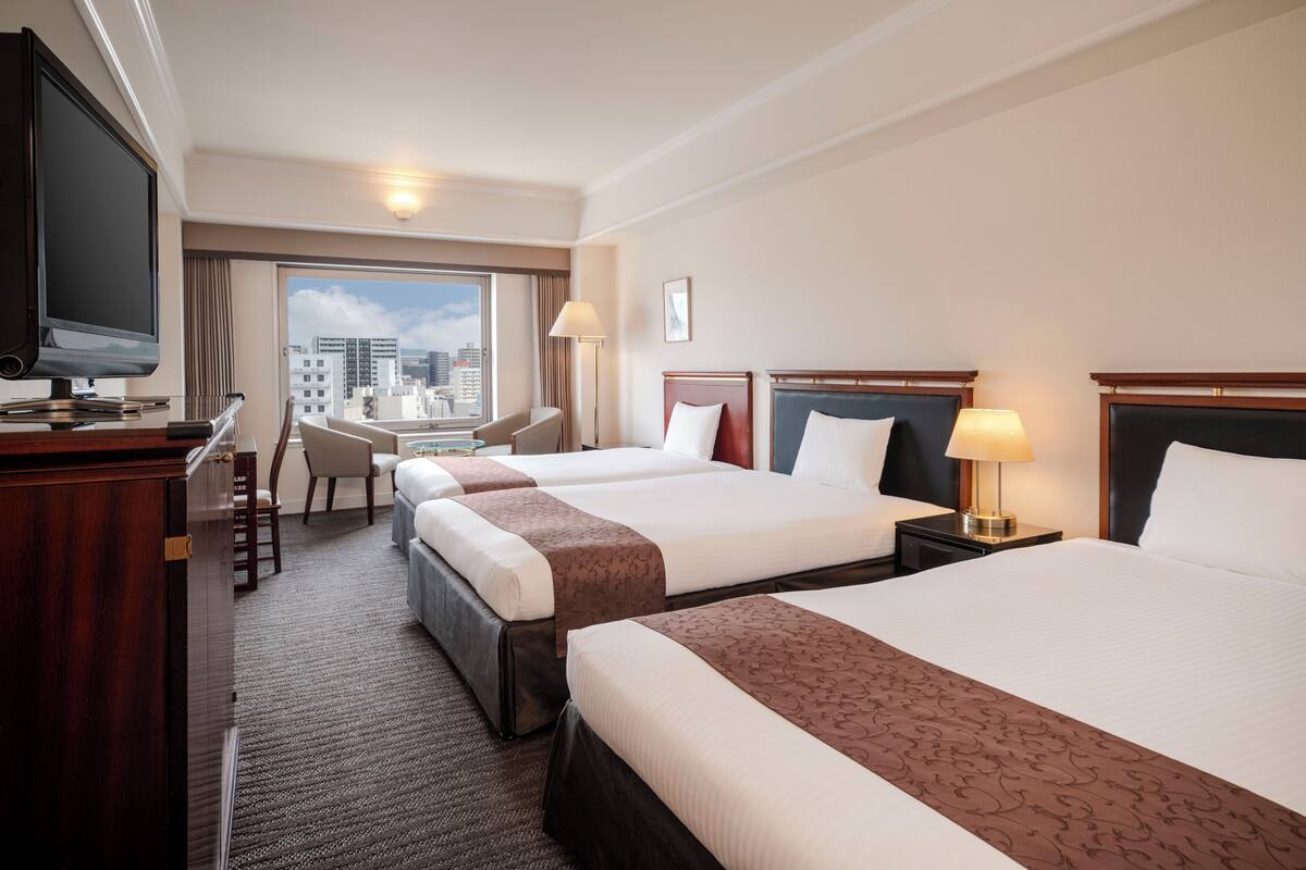 Une chambre d’hôtel avec deux lits, un bureau, une télévision et une vue sur la ville.