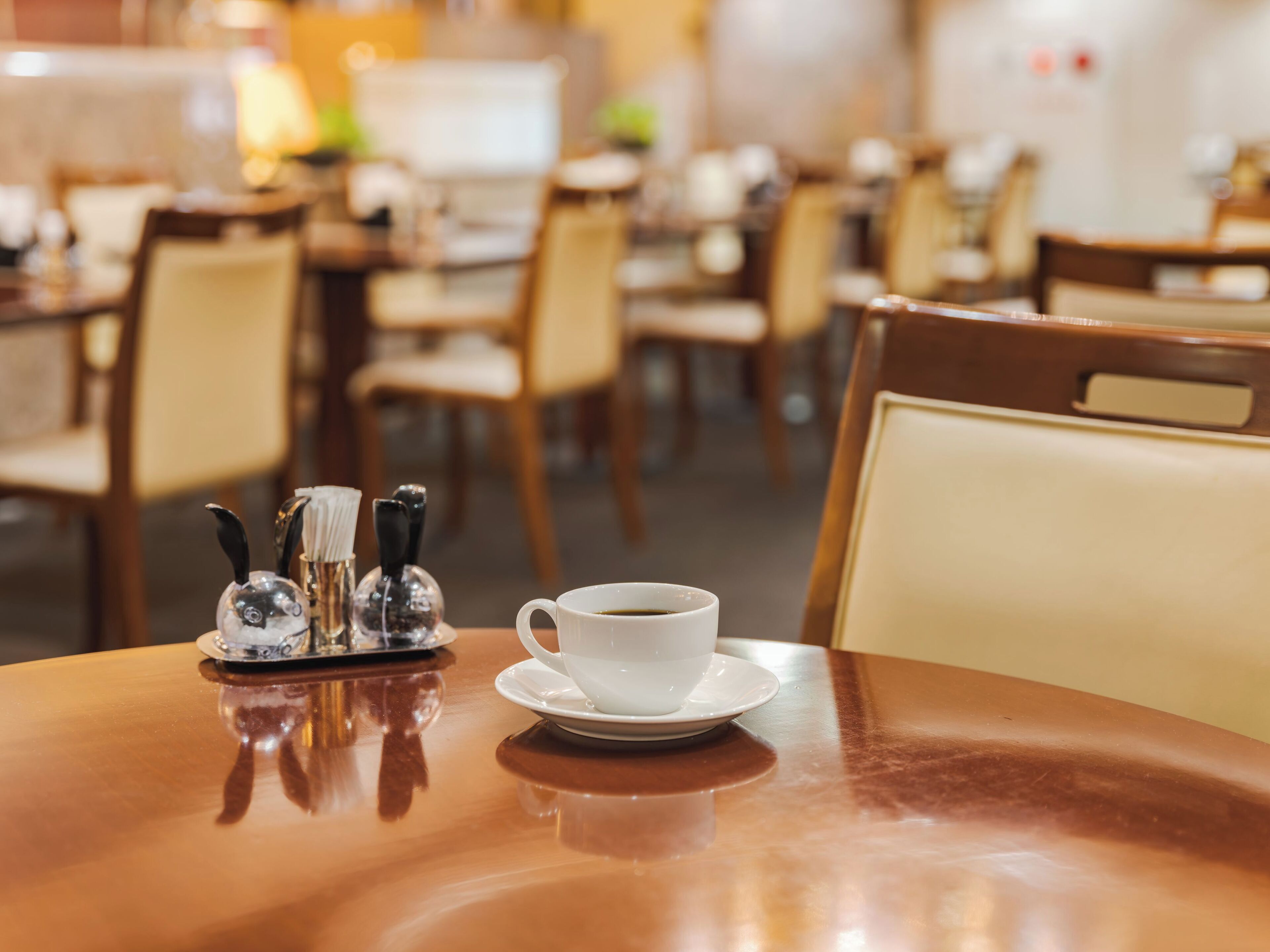 Ein Esstisch mit einer Kaffeetasse, Salz- und Pfefferdose sowie Stühlen in einem Restaurant.