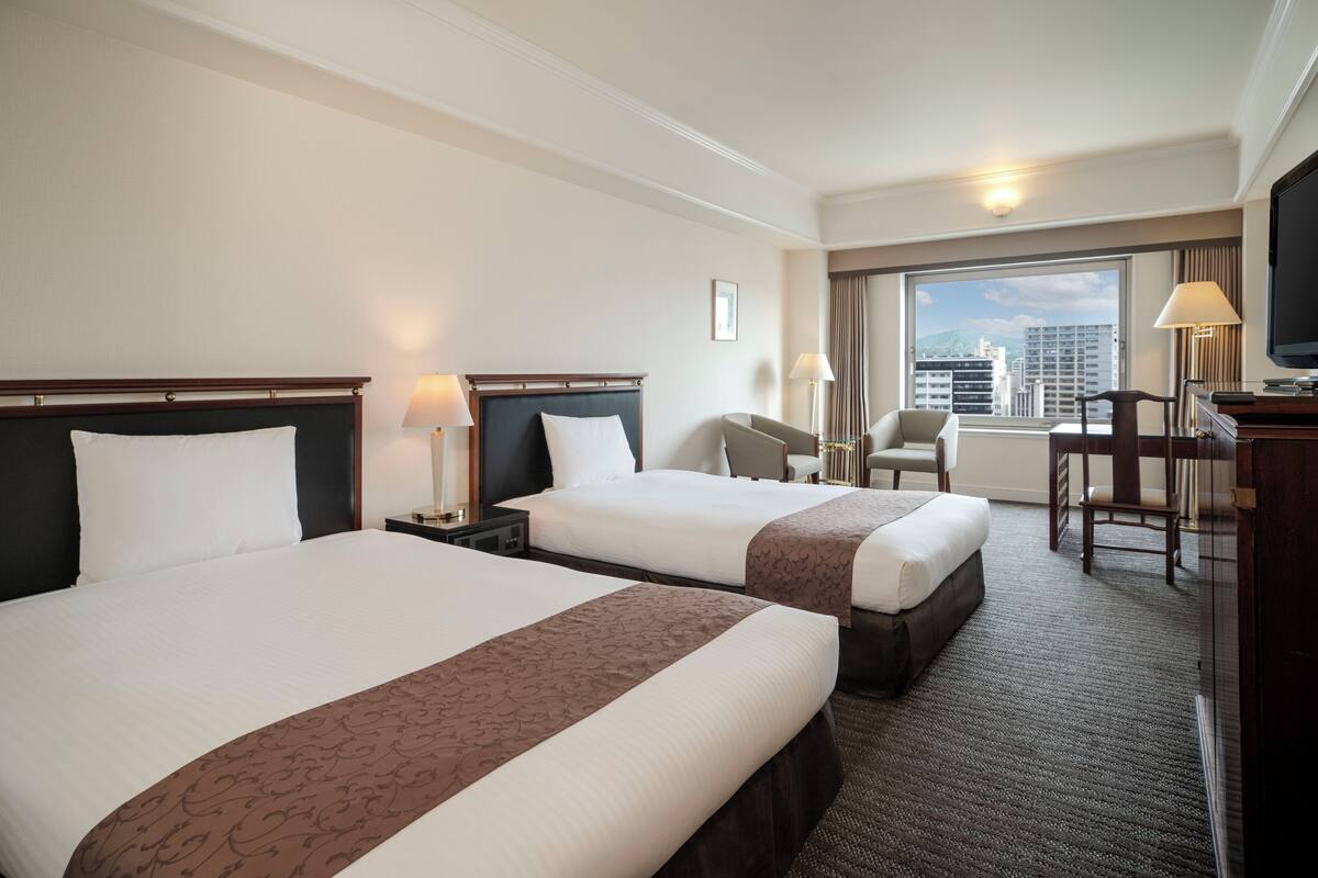 Une chambre d’hôtel avec deux lits, un bureau, une chaise, une télévision et une vue sur la ville.
