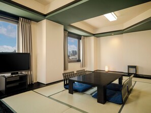 A hotel room with tatami flooring, a large flat-screen TV, a dining table with chairs, and a city view.