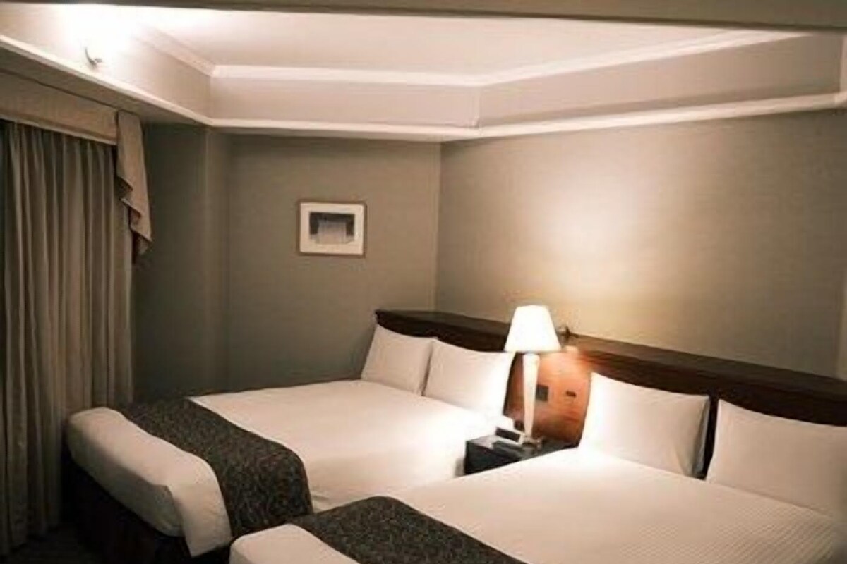 Een hotelkamer met twee bedden, een nachtkastje, een lamp en een raam met gordijnen.