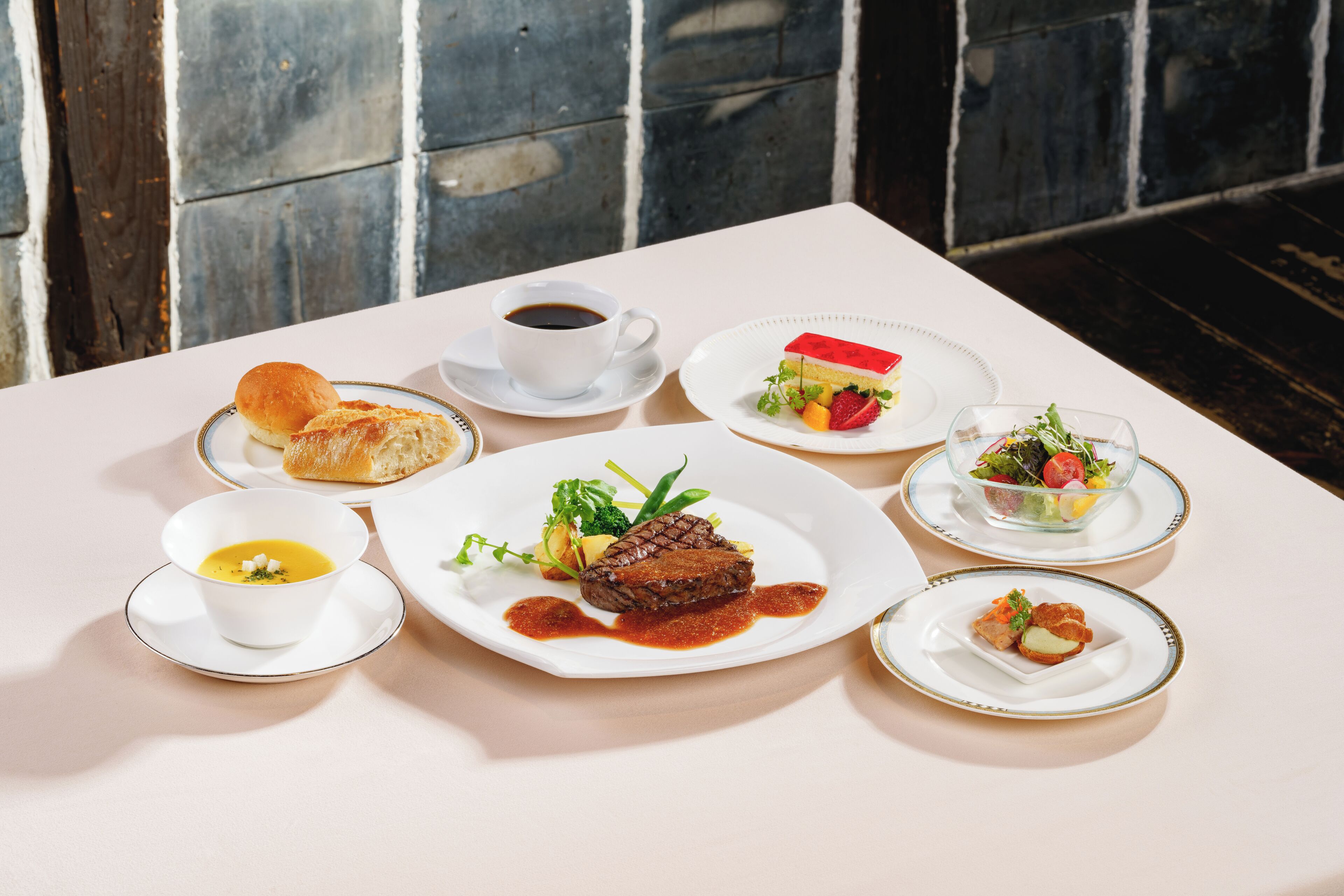 Una mesa servida con diversos platos, incluyendo sopa, carne, ensalada y pan.