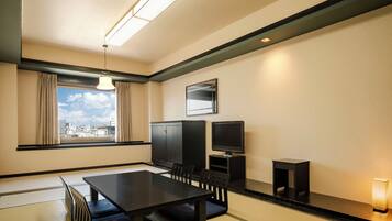 A hotel room with tatami flooring, a dining table with chairs, a television, a cabinet, and a window with curtains.