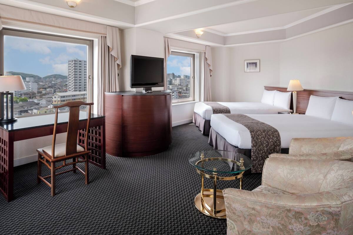 Une chambre d’hôtel avec un lit, un bureau avec une télévision, une chaise, un canapé et une vue sur la ville.