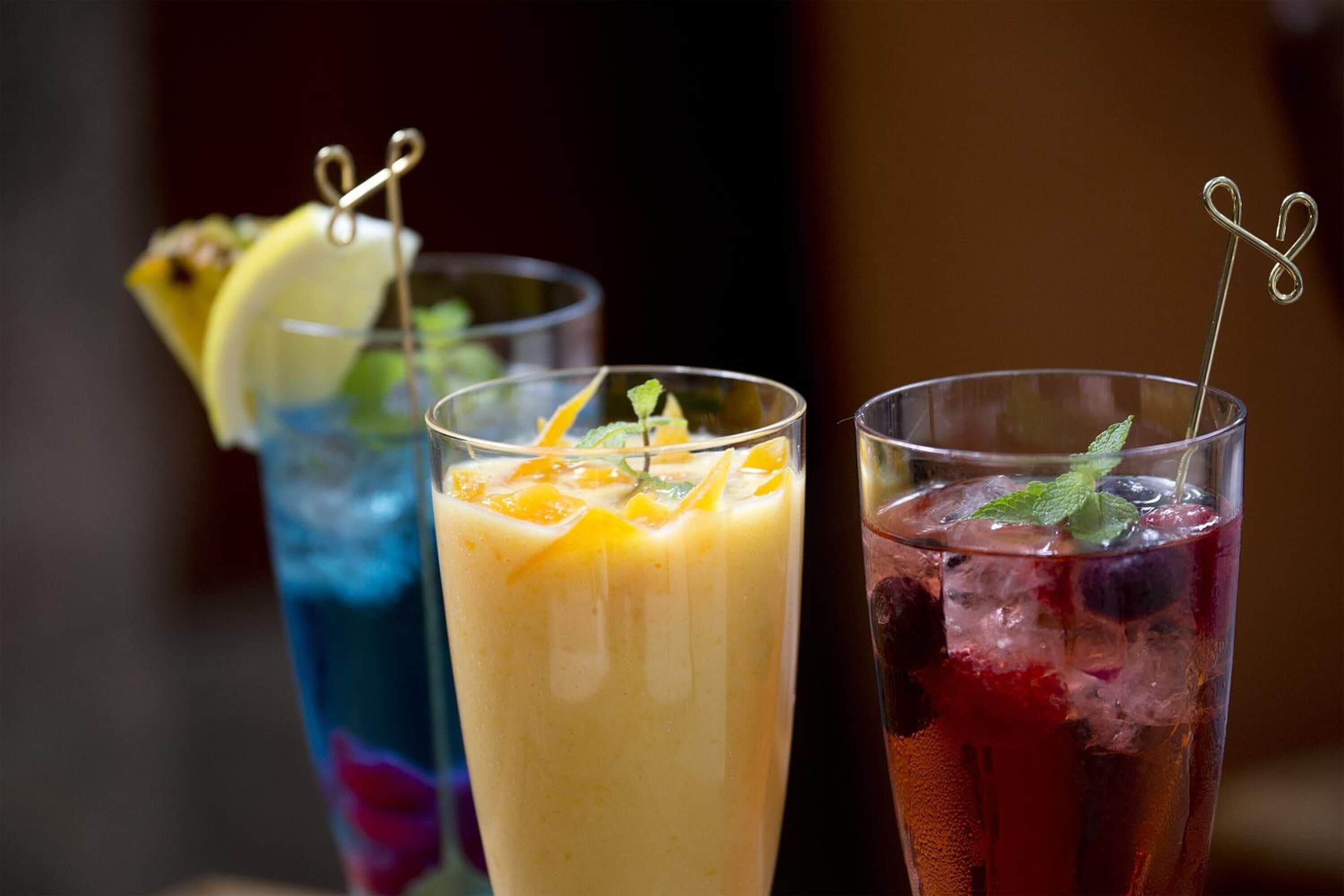 Three glasses of beverages with garnishes and straws.