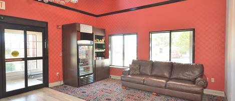 A spacious living room with a brown leather sofa, a vending machine, and a patterned carpet.