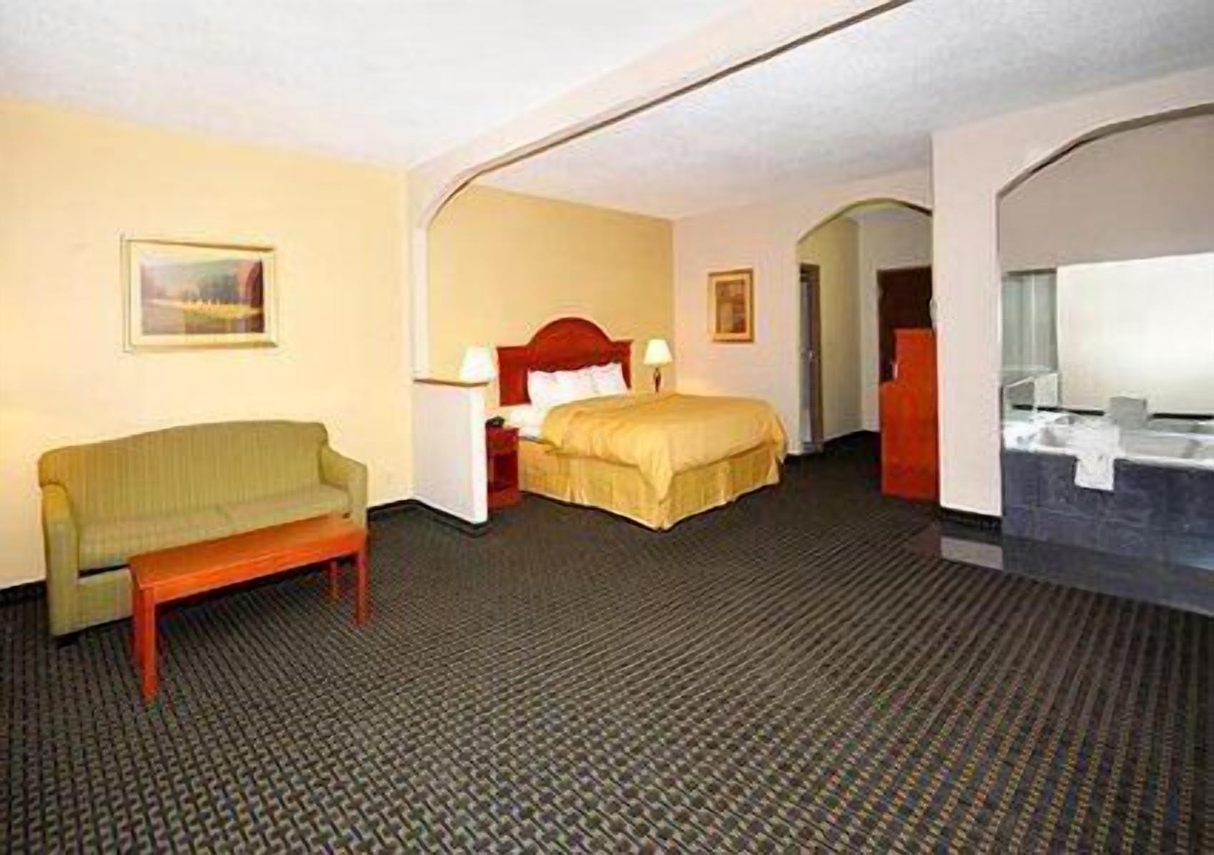 A hotel room with a bed, a sofa, a desk, a chair, and a bathroom with a sink and mirror.