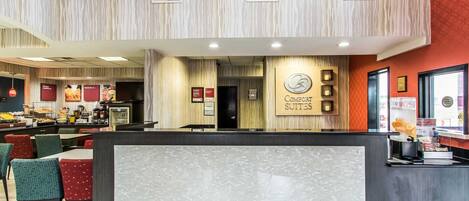 A hotel reception area with a modern design, including a reception desk, seating area, and a view of the dining section.