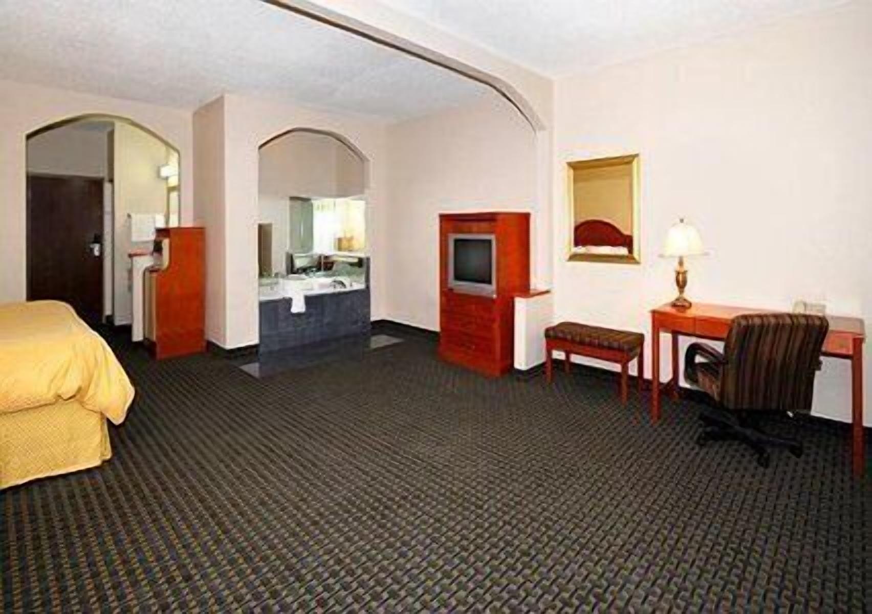 Habitación de hotel con cama, escritorio, silla, televisión, espejo y baño con lavabo y espejo.