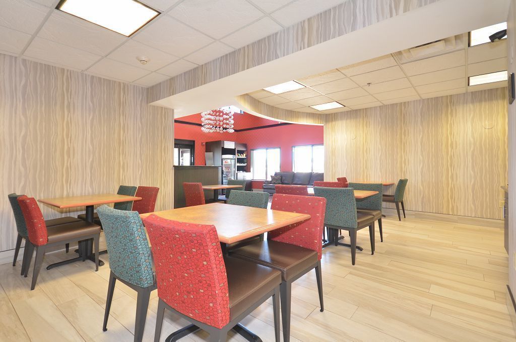 A dining area with multiple tables and chairs, a kitchen in the background, and a patterned wall.