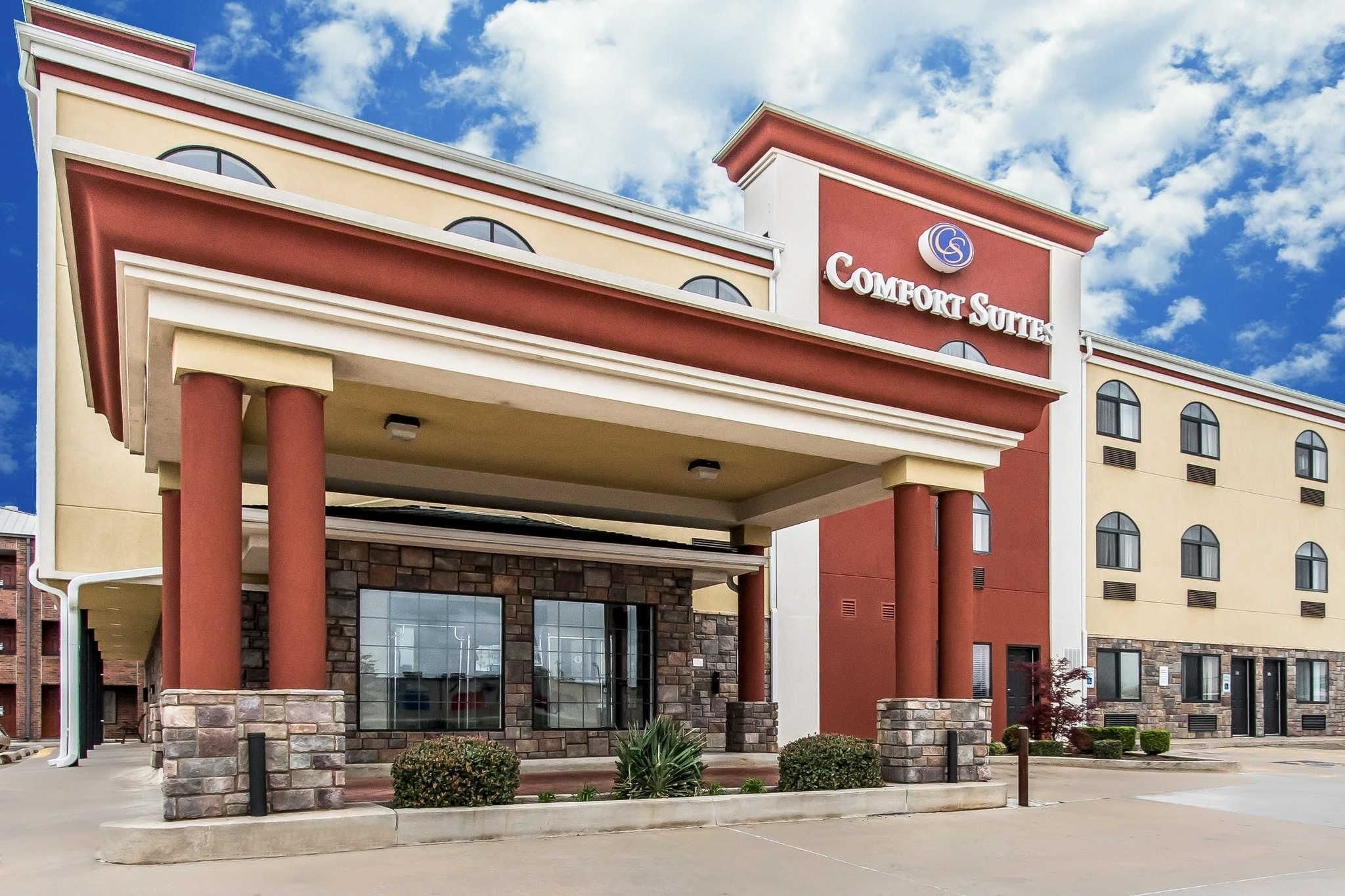 Un hôtel à la façade rouge et beige, doté de grandes fenêtres et d’une enseigne bien visible indiquant « Comfort Suites ».