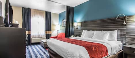 Habitación de hotel con una cama grande, un escritorio con computadora, televisor y ventana con cortinas.