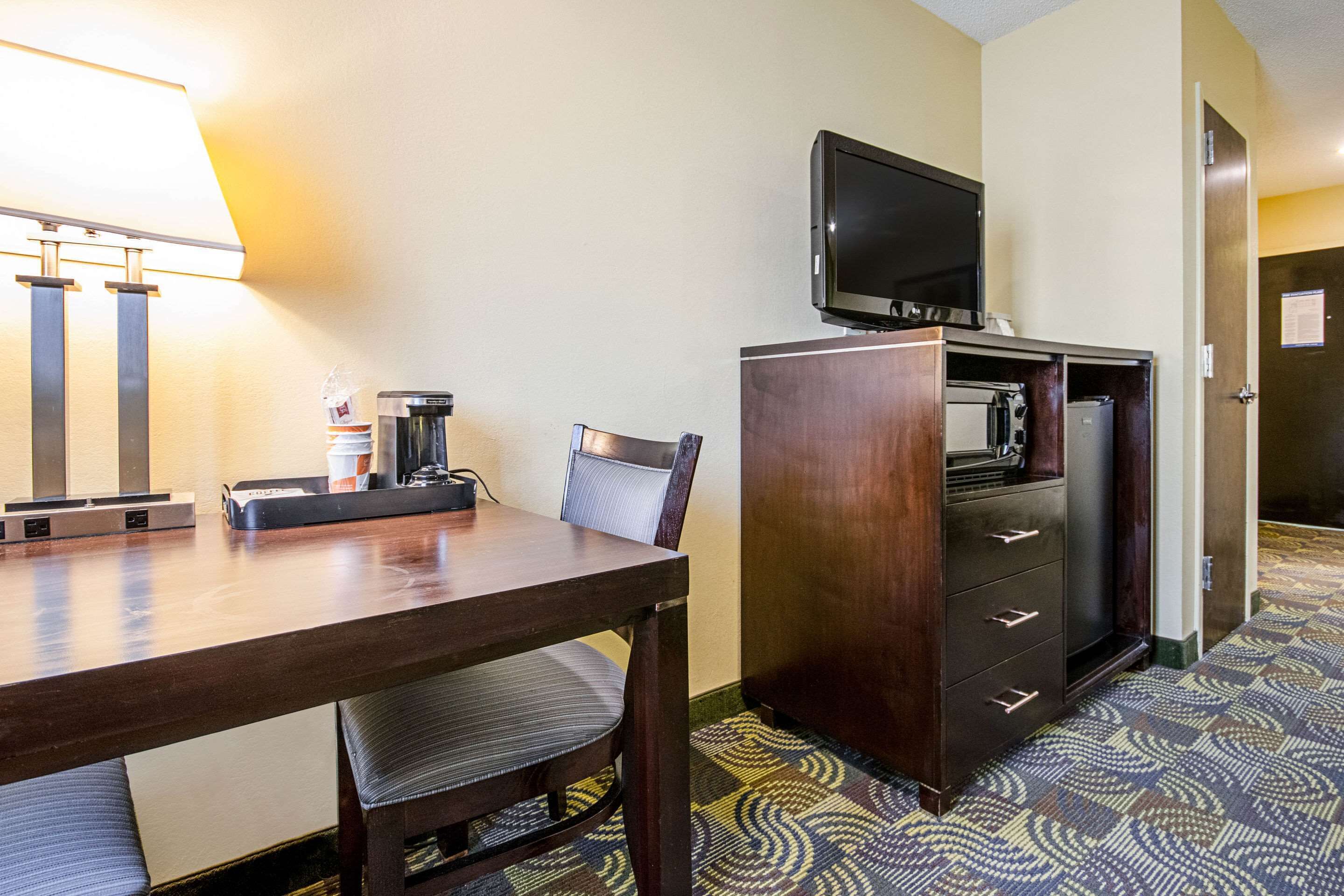 Een hotelkamer met een houten bureau, een stoel, een televisie op een kast, een lamp en een kamerbreed tapijt met een patroon.