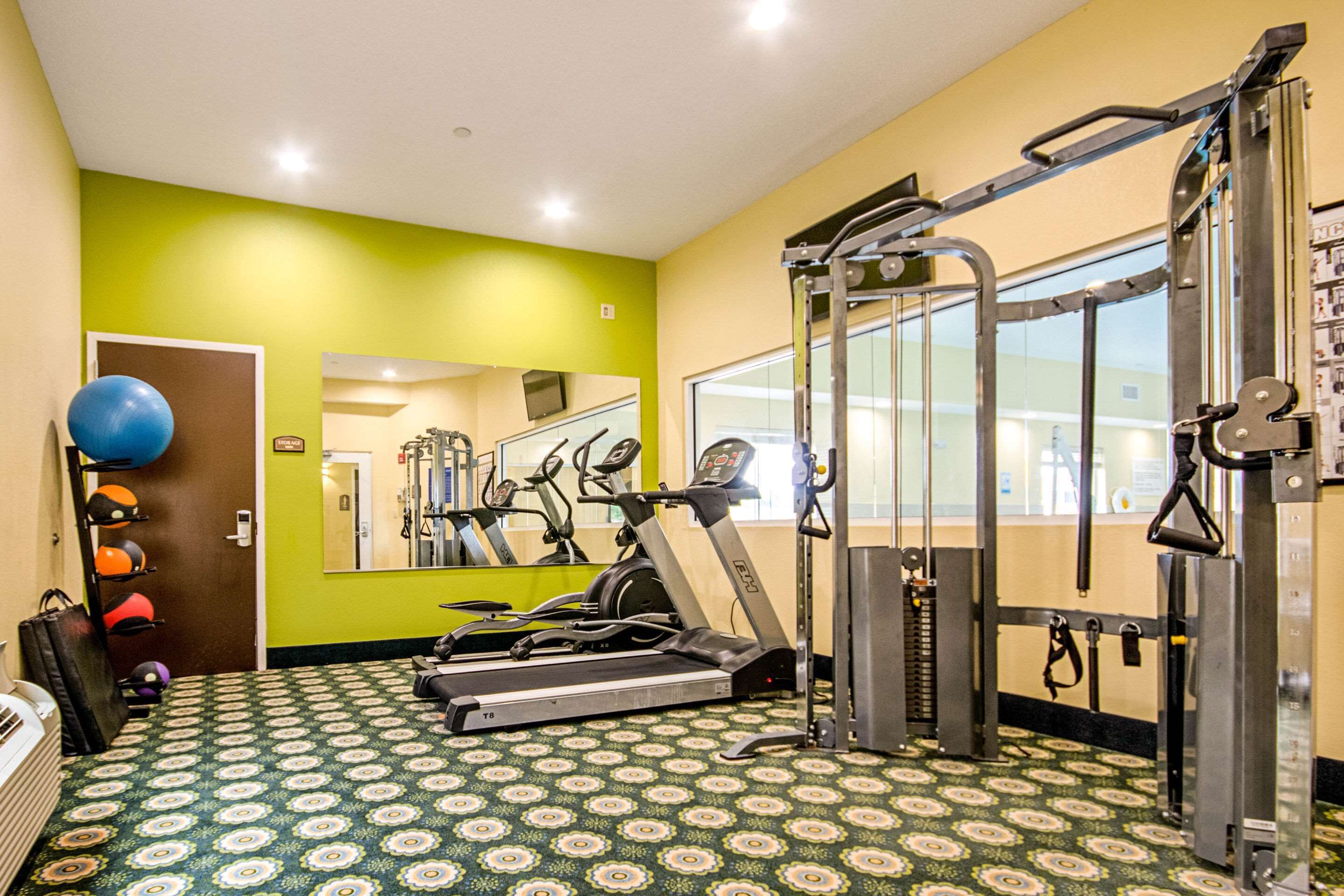 Ett gym med träningsutrustning, ett mönstrat golv och en spegel.