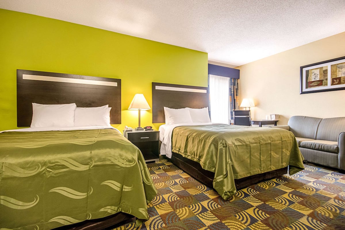 A hotel room with two beds, a sofa, and a patterned carpet.
