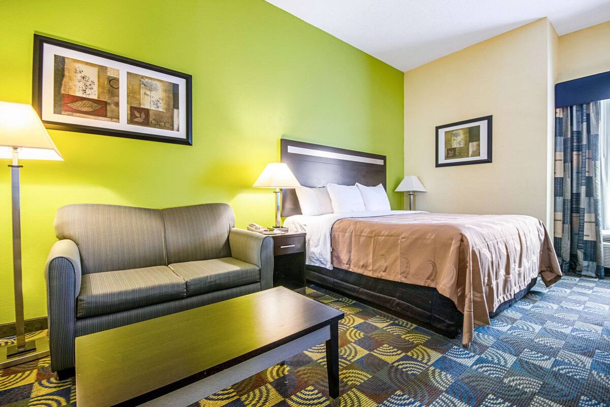 A hotel room with a bed, a sofa, a nightstand, and a table.