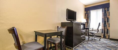 A hotel room with a desk, two chairs, a television, a desk lamp, and a patterned carpet.