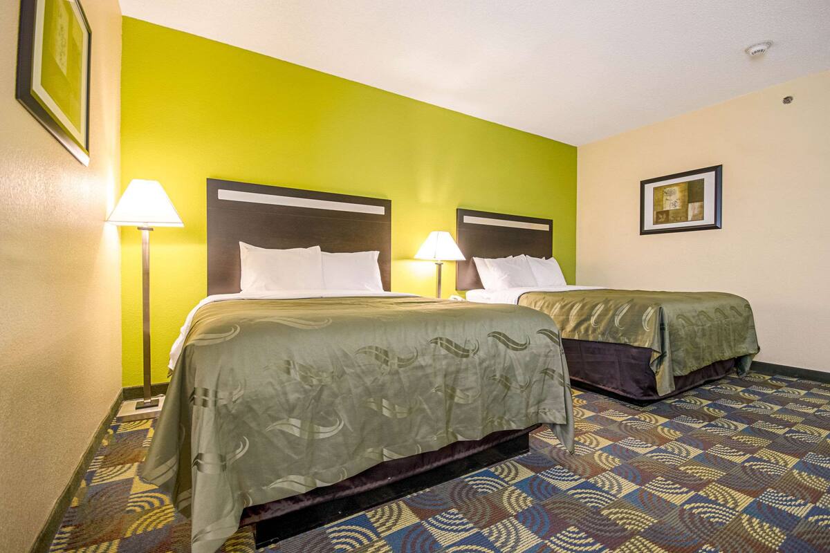 A hotel room with two beds, each with a headboard, a patterned carpet, and a green wall.