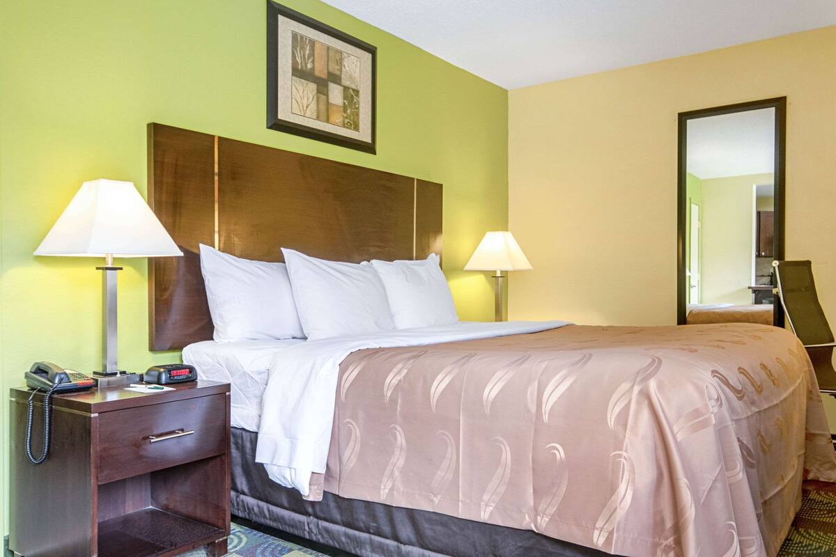 A hotel room with a bed, two bedside lamps, a nightstand with a telephone, and a mirror.