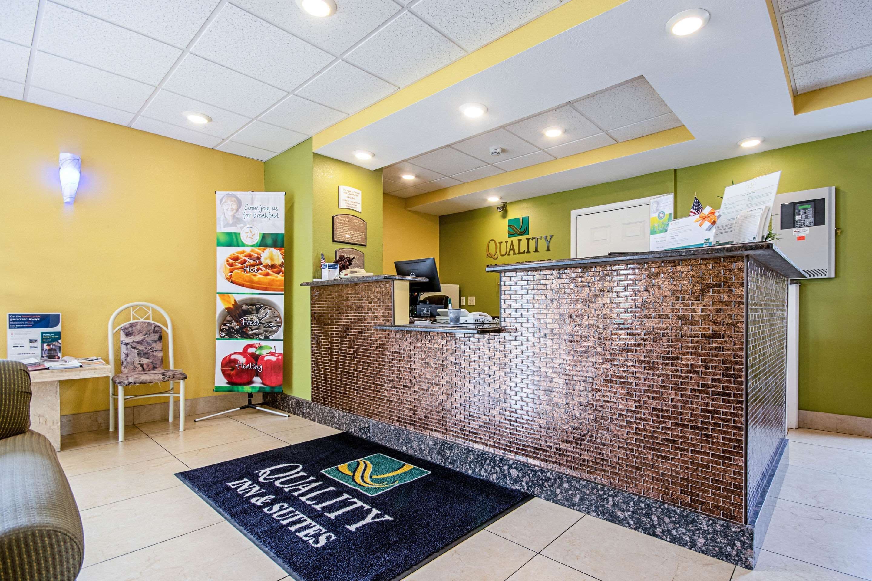 A reception area with a brick wall, a reception desk, a chair, a desk with a computer, and a wall-mounted phone.