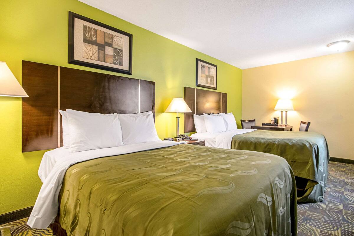 A hotel room with two beds, green walls, and framed artwork above the beds.