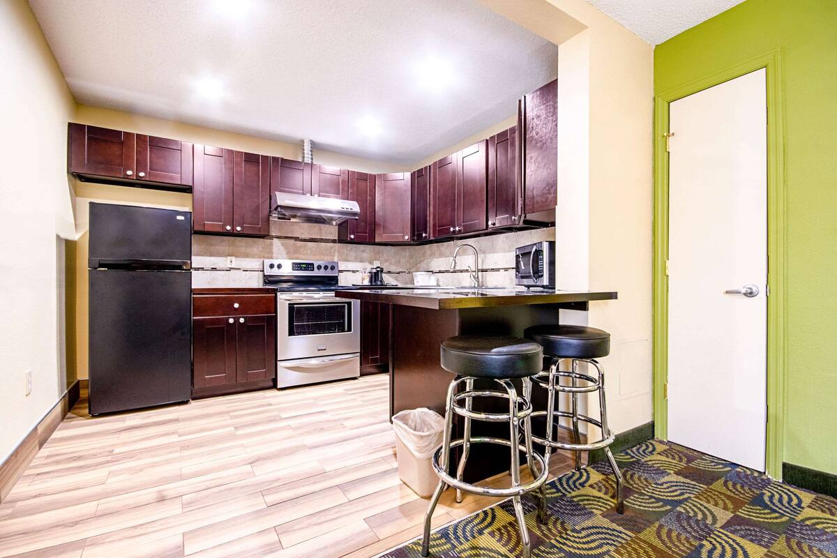A kitchen with dark wooden cabinets, a stainless steel refrigerator, an oven, a microwave, and a bar stool area.