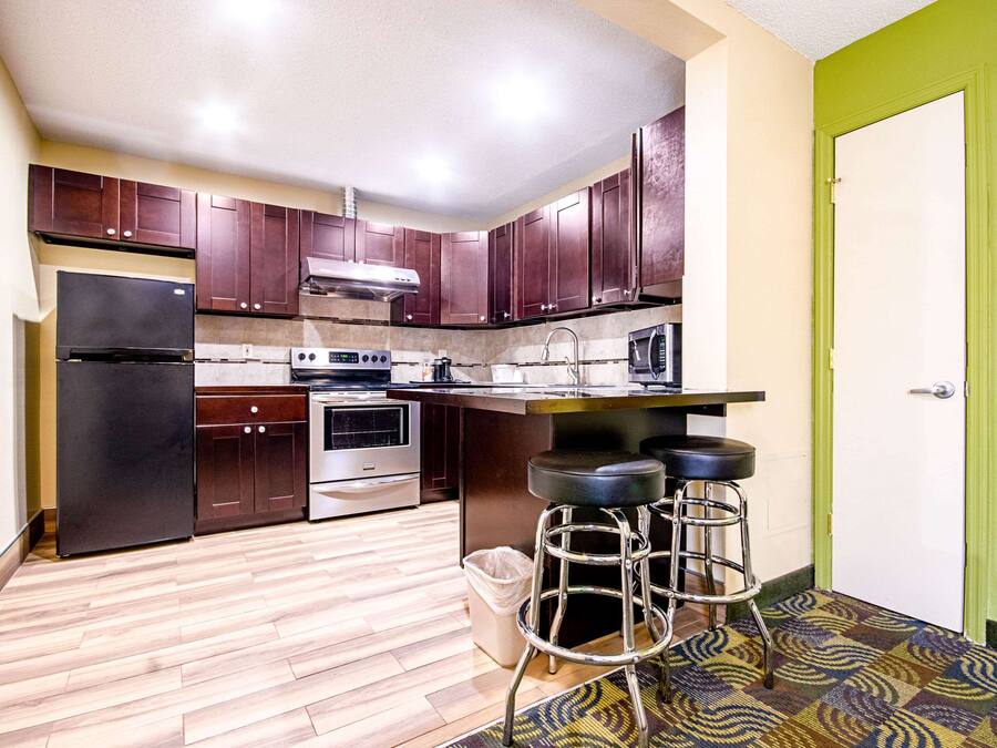A kitchen with dark wooden cabinets, a stainless steel refrigerator, an oven, a microwave, and a bar stool area.