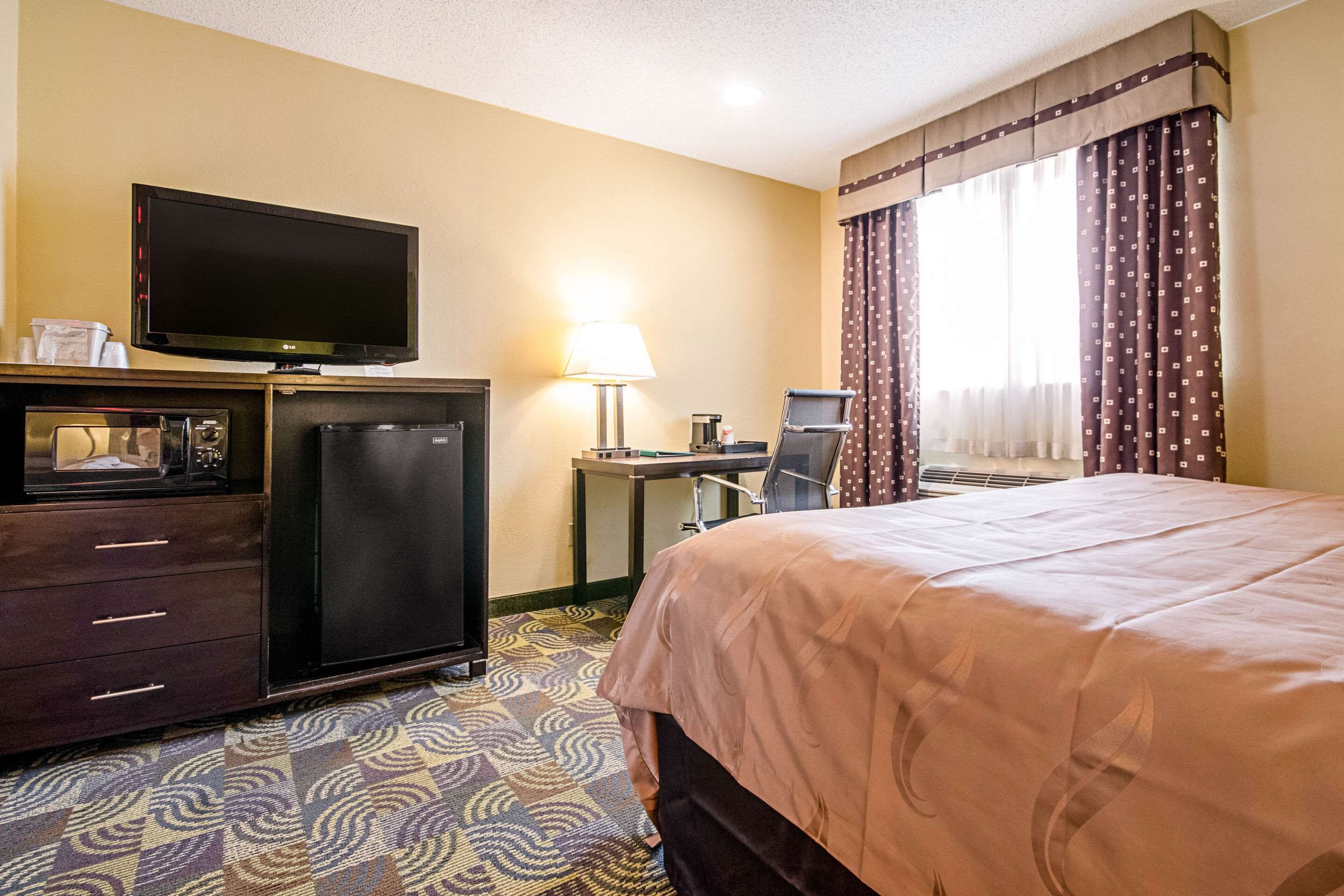 A hotel room with a bed, a television, a refrigerator, a desk, and a lamp.