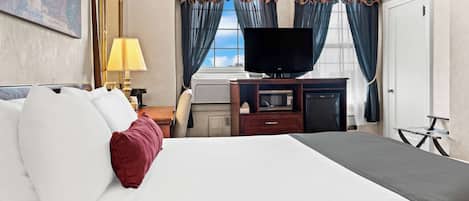 Habitación de hotel con una cama grande, una televisión de pantalla plana, un escritorio con lámpara y una ventana con cortinas.