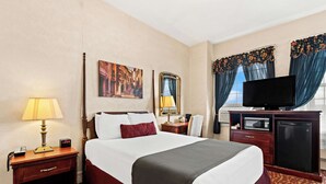 A hotel room with a bed, a desk with a lamp, a television, and a microwave. - Genetti Hotel, SureStay Collection by Best Western (Williamsport)