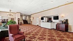 A spacious lobby with a patterned carpet, a red upholstered chair, a reception desk, and a television. - Genetti Hotel, SureStay Collection by Best Western (Williamsport)