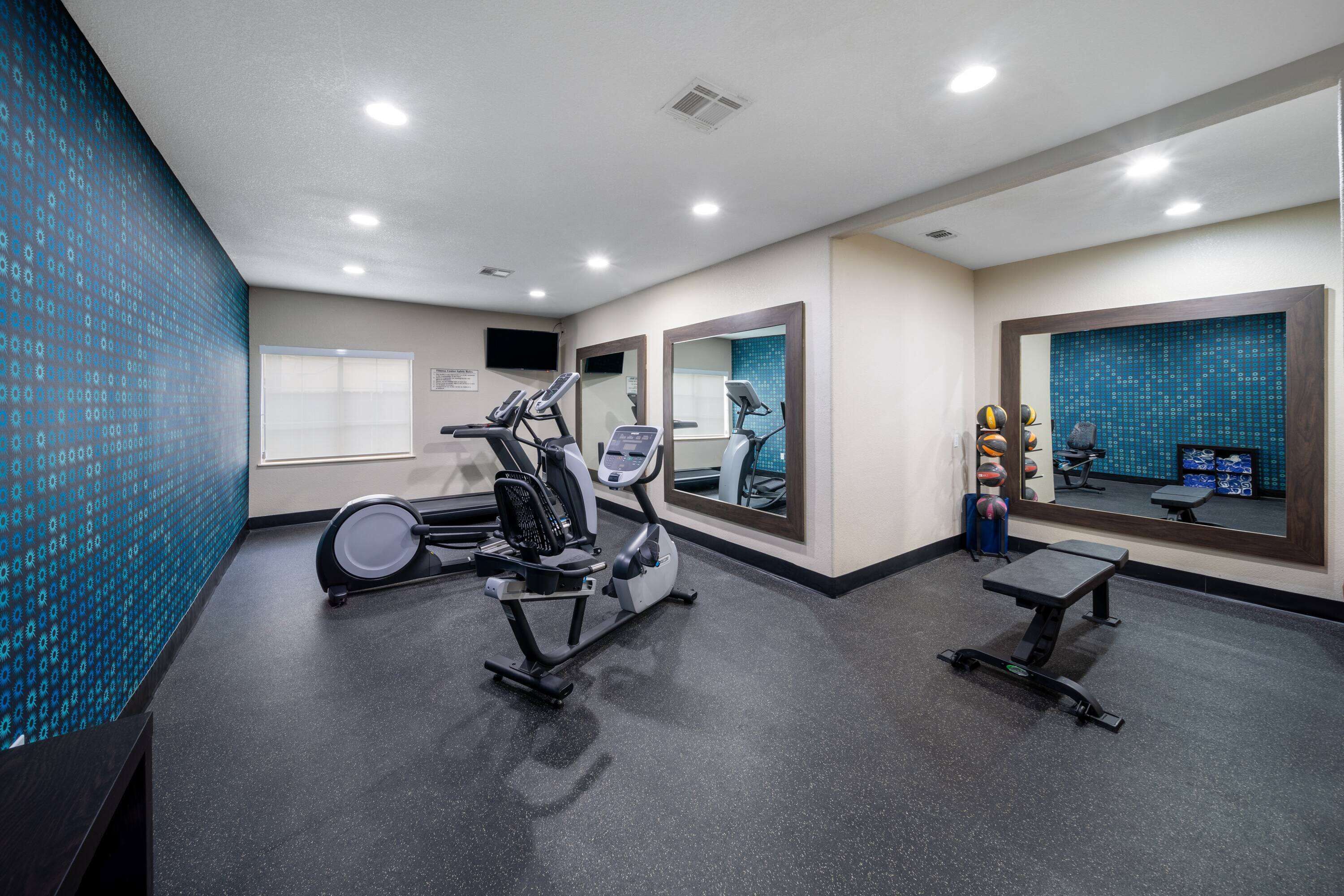 Un gimnasio con cintas de correr, elípticas y un banco.