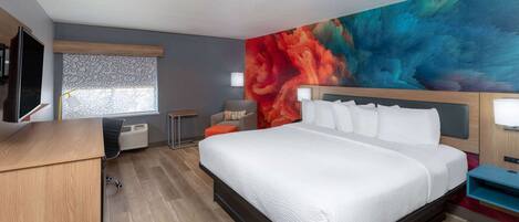 A modern hotel room with a large bed, a desk, a chair, a flat-screen TV, and a colorful mural on the wall.