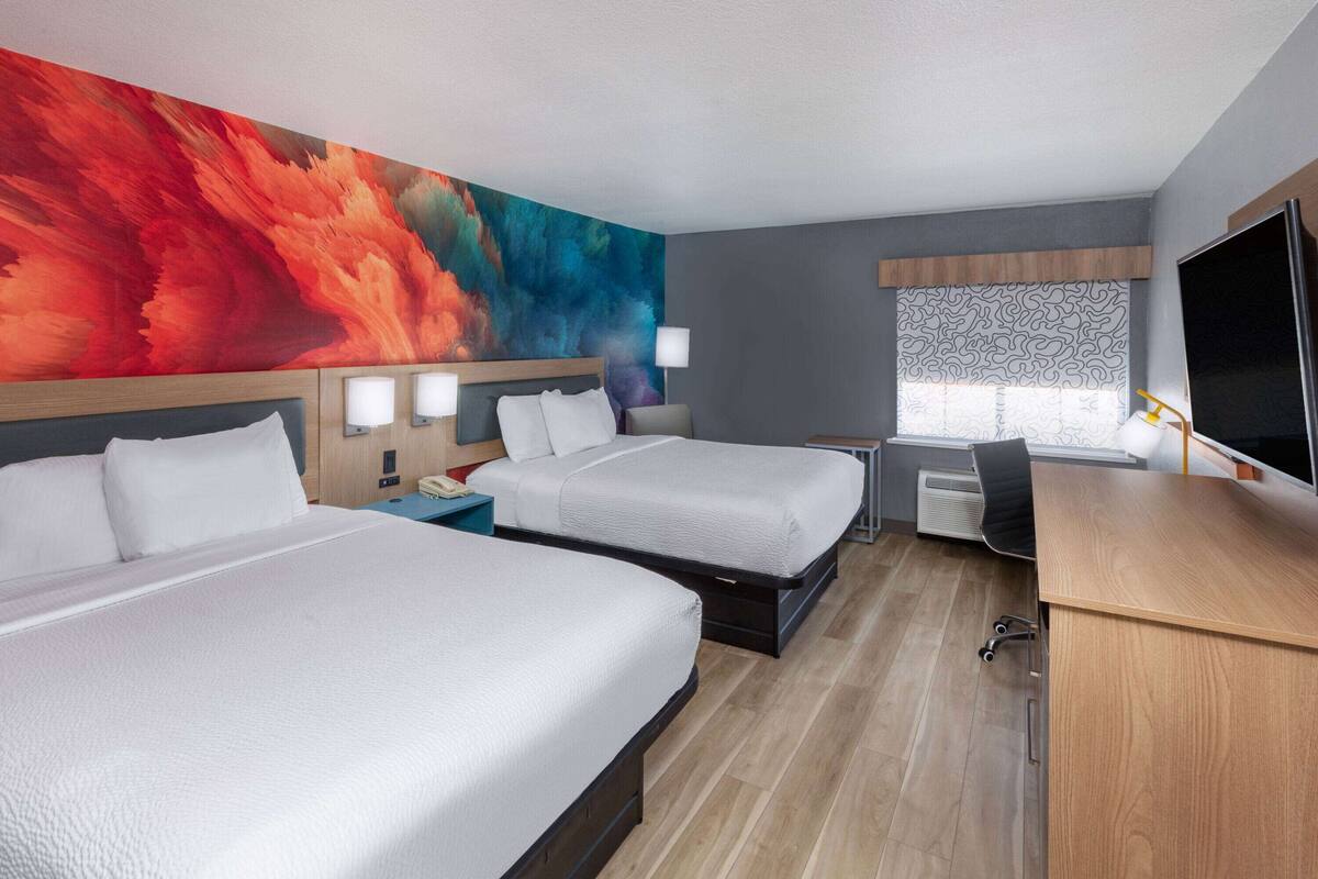 A hotel room with two beds, a desk, a TV, and a large abstract painting on the wall.