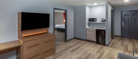 Habitación de hotel pequeña con televisor, cómoda de madera, kitchenette y una puerta.